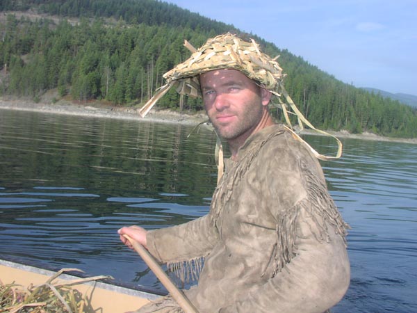 Thomas Elpel in Buckskins and Cattail Hat canoeing on lake.